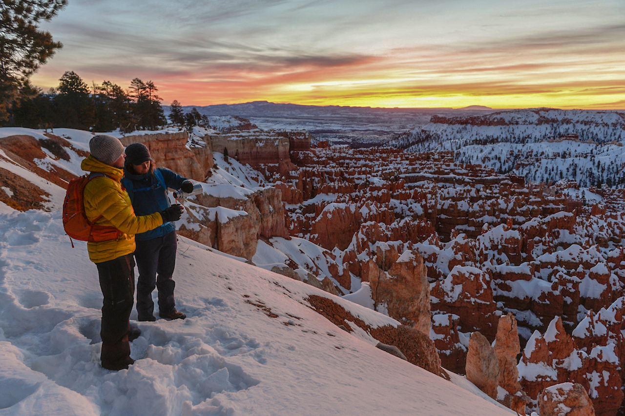 Ein Paar betrachtet den Sonnenuntergang am verschneiten Sunset Point im Bryce Canyon