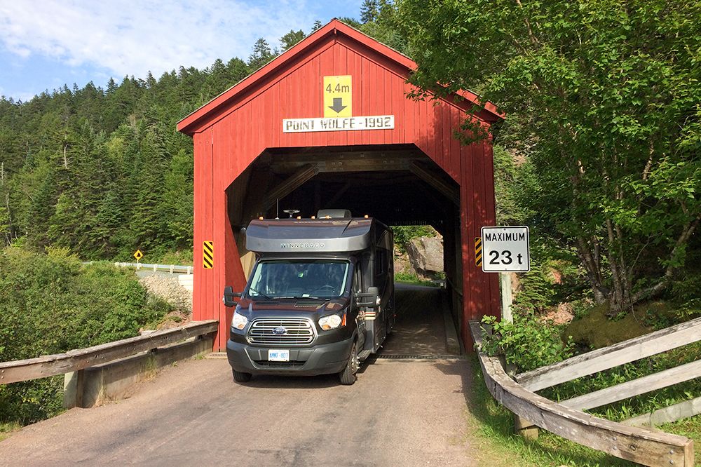 Ein C23 Fuse Camper von Owasco RV fÃ¤hrt durch eine gedeckte BrÃ¼cke in der USA