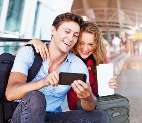 Ein Pärchen verwendet am Flughafen eine Reise-App auf ihrem Handy Ein Pärchen verwendet am Flughafen eine Reise-App auf ihrem Handy
