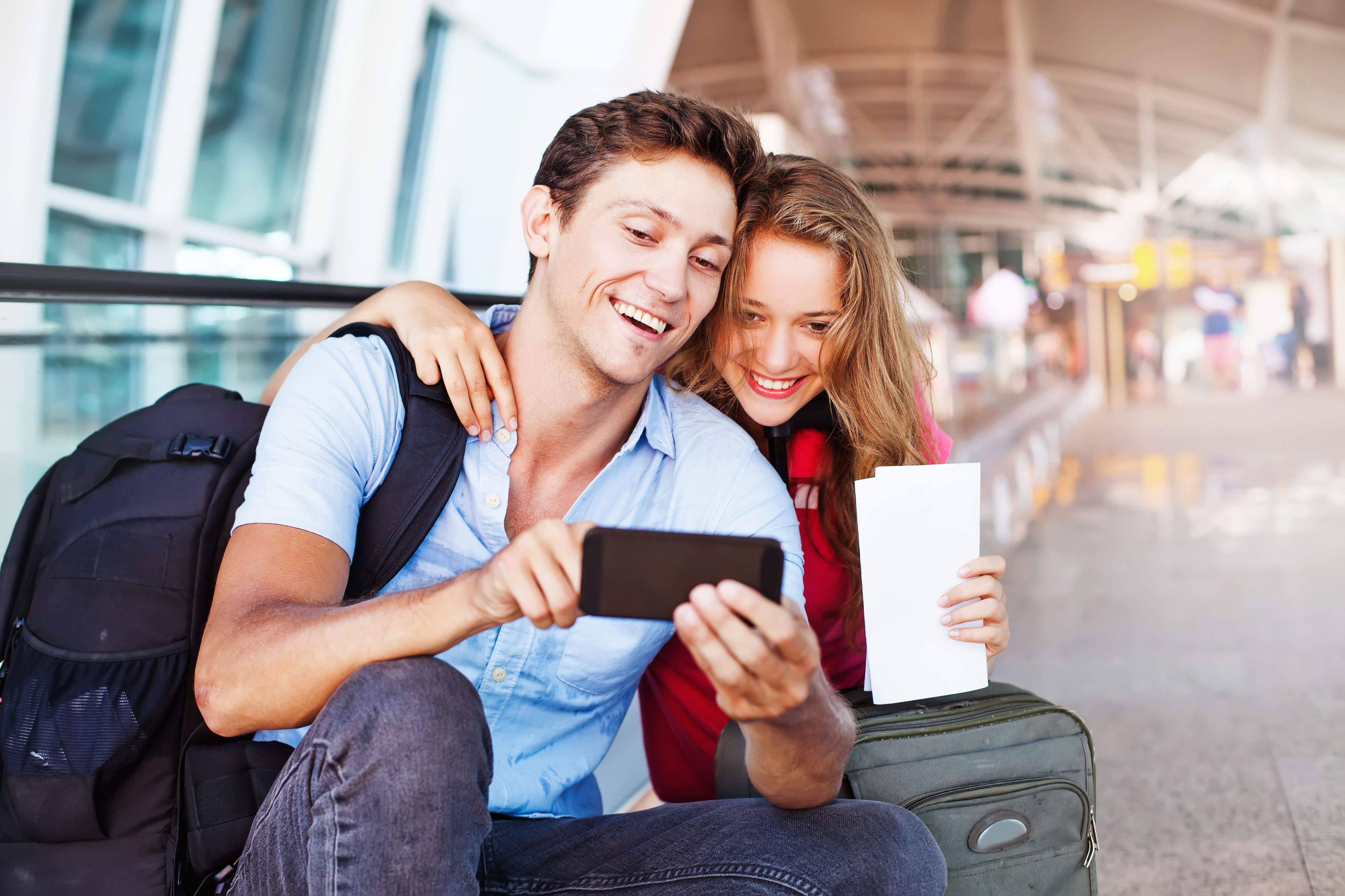 Paar am Flughafen mit Handgepäck und Reise-App auf dem Handy