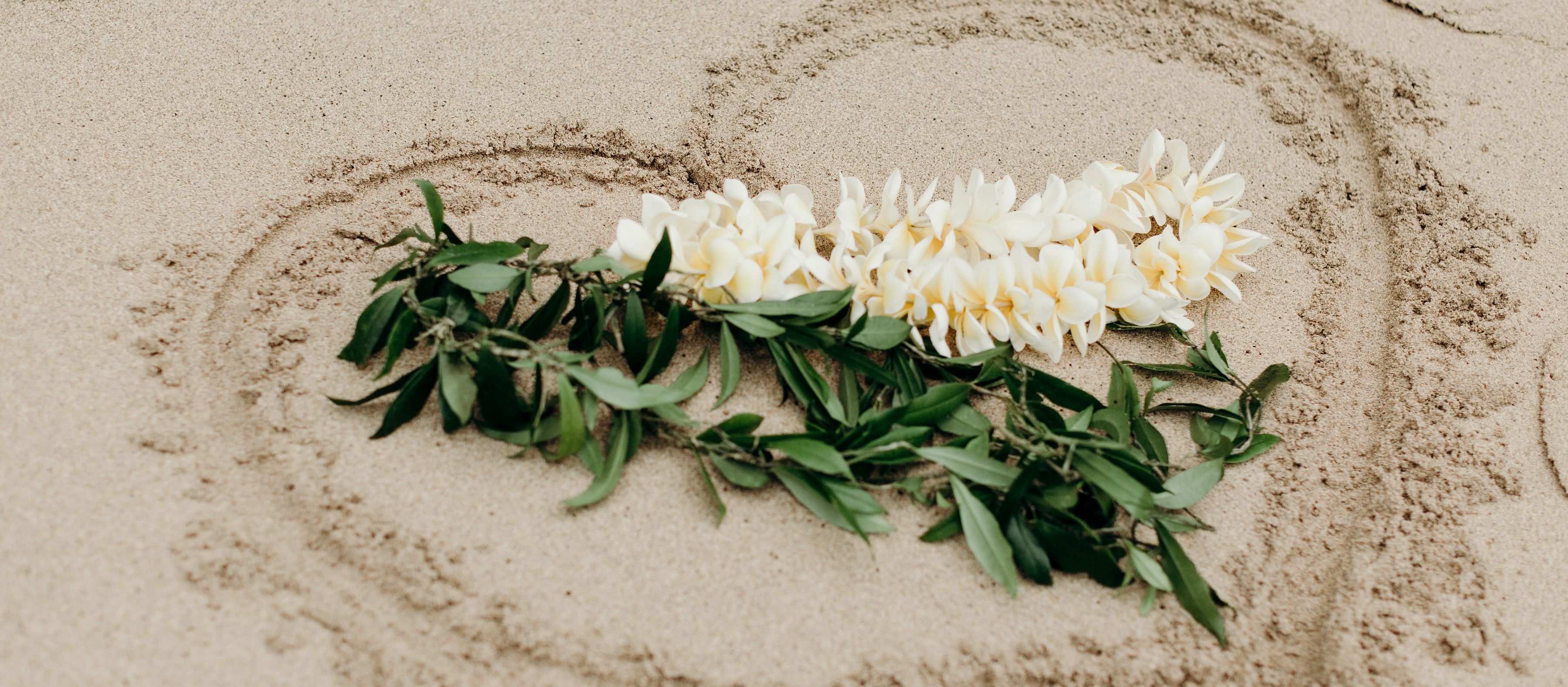 Hawaiischer Hochzeitsschmuck auf ein Herz im Sand gelegt
