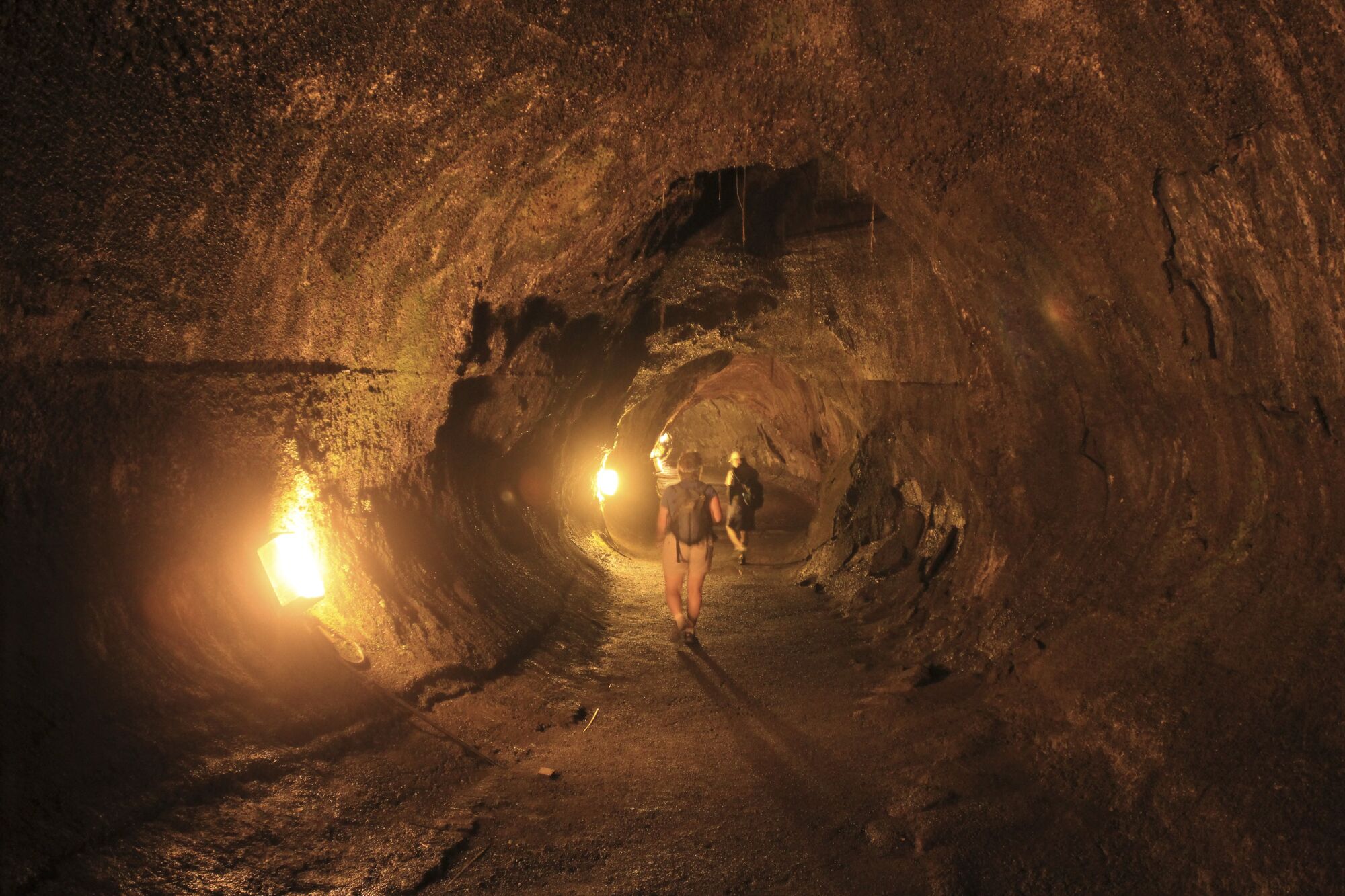 Menschen wandern durch eine beleuchtete Lavahöhle mit natürlichen Felswänden.