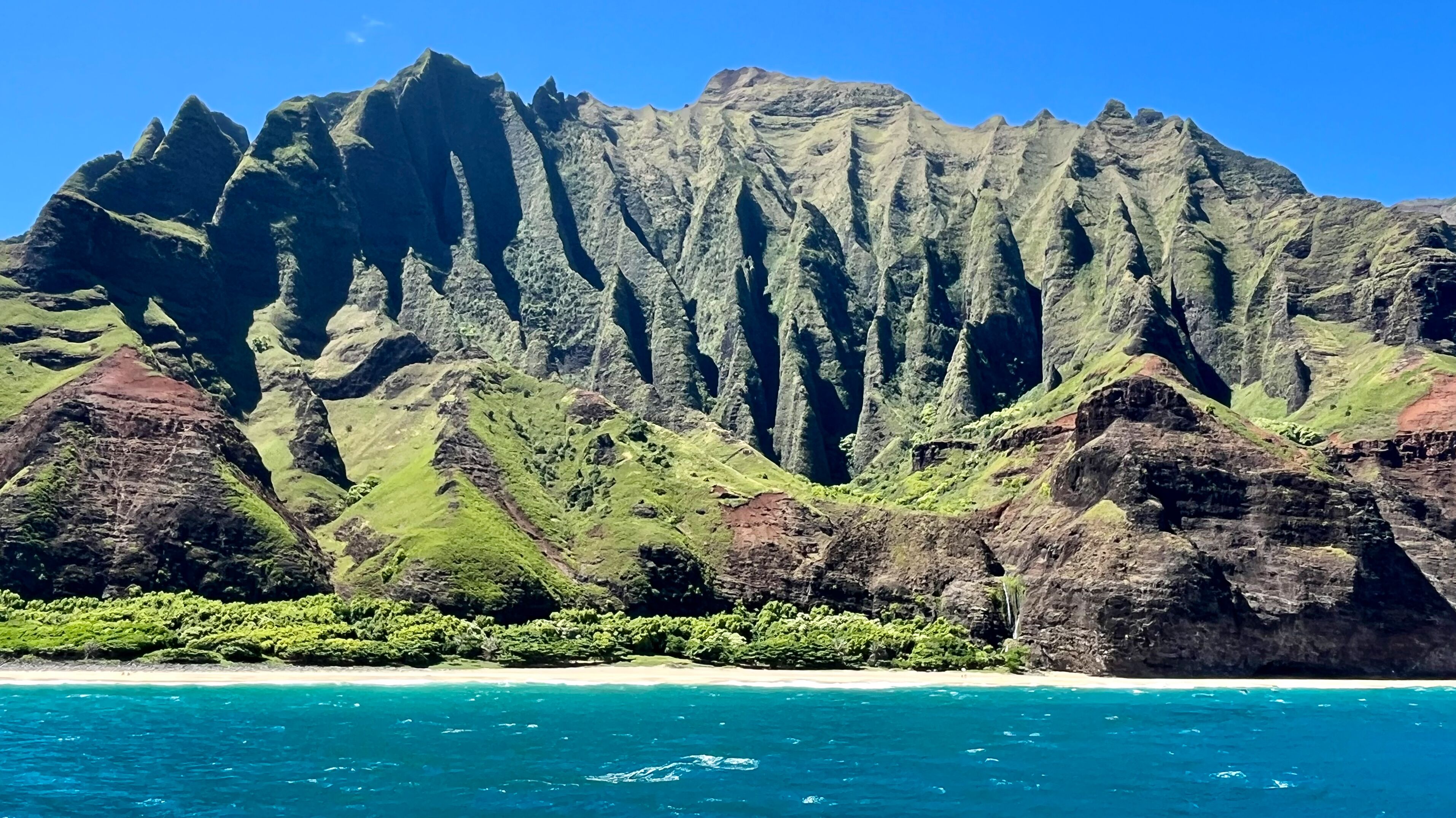 Zerklüftete Berge mit grüner Vegetation, schönem Sandstrand und türkisblauem Meer.