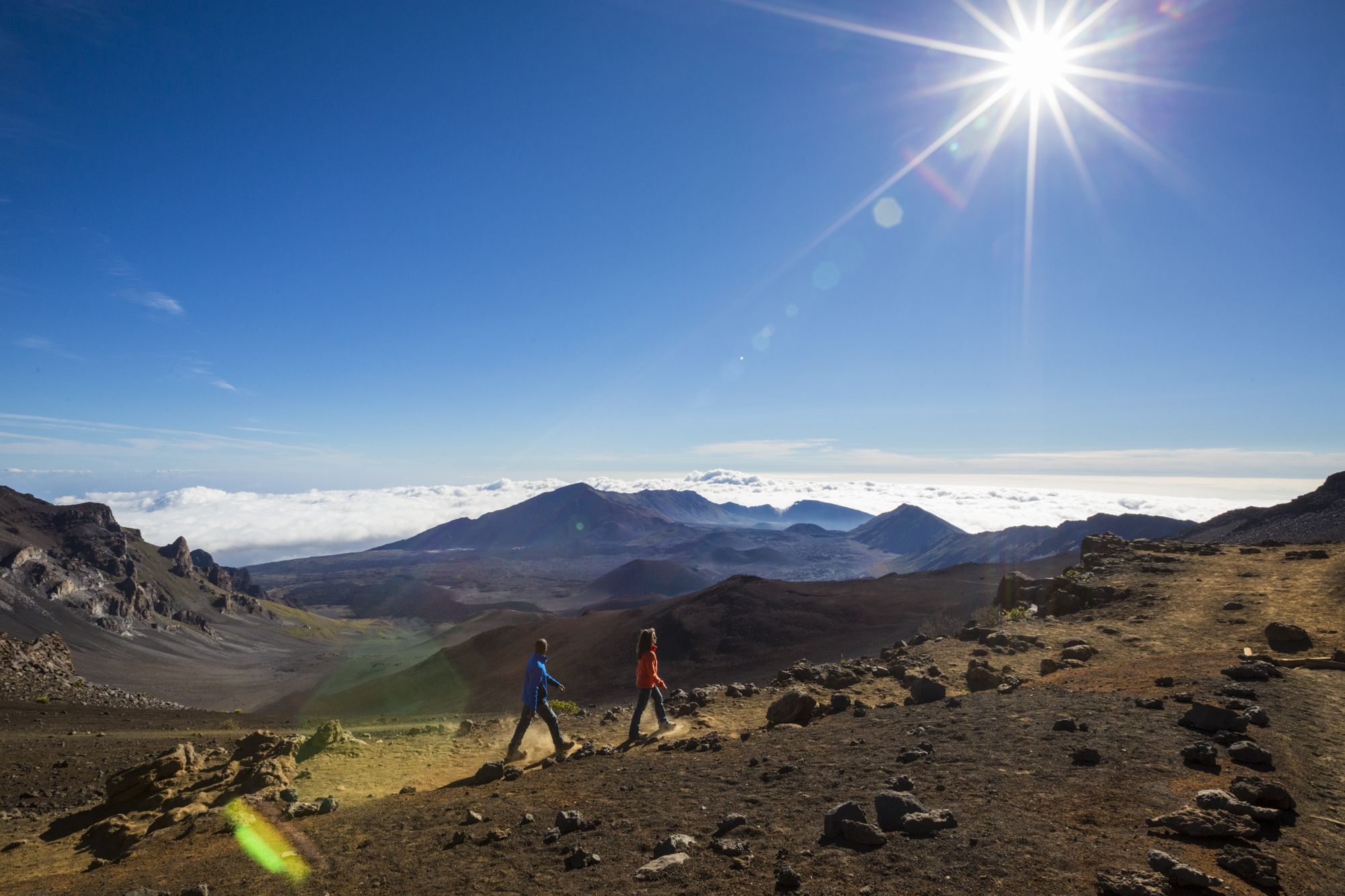 Ein Pärchen wandert unter strahlend blauem Himmel durch die raue Landschaft des Haleakala-Vulkans.