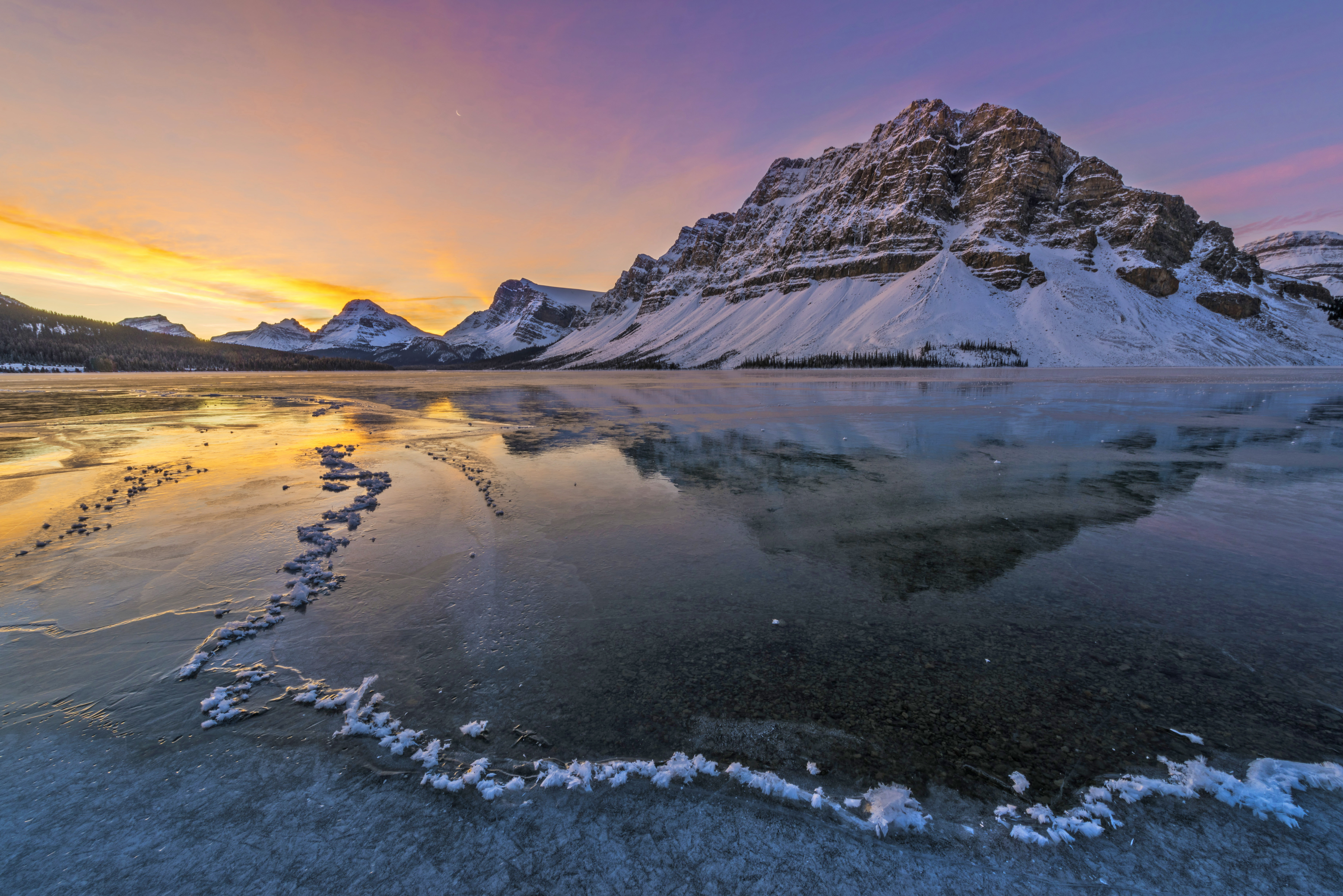 Farbenfroher Sonnenaufgang über dem eisigen Bow Lake im Banff National Park, Alberta