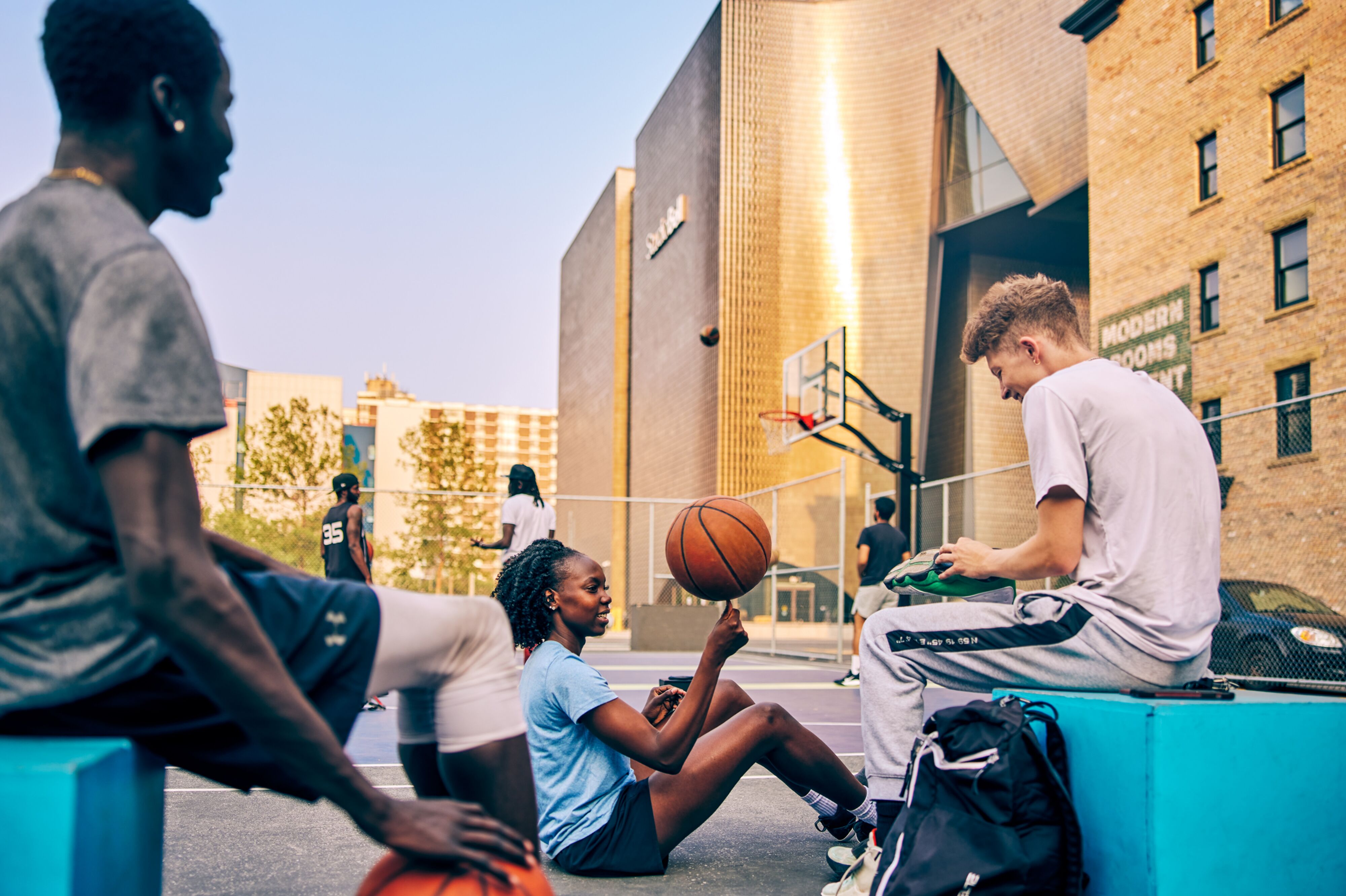 Eine Gruppe Jugendlicher sitzt auf einem Basketballplatz, einer dreht einen Basketball auf dem Finger.