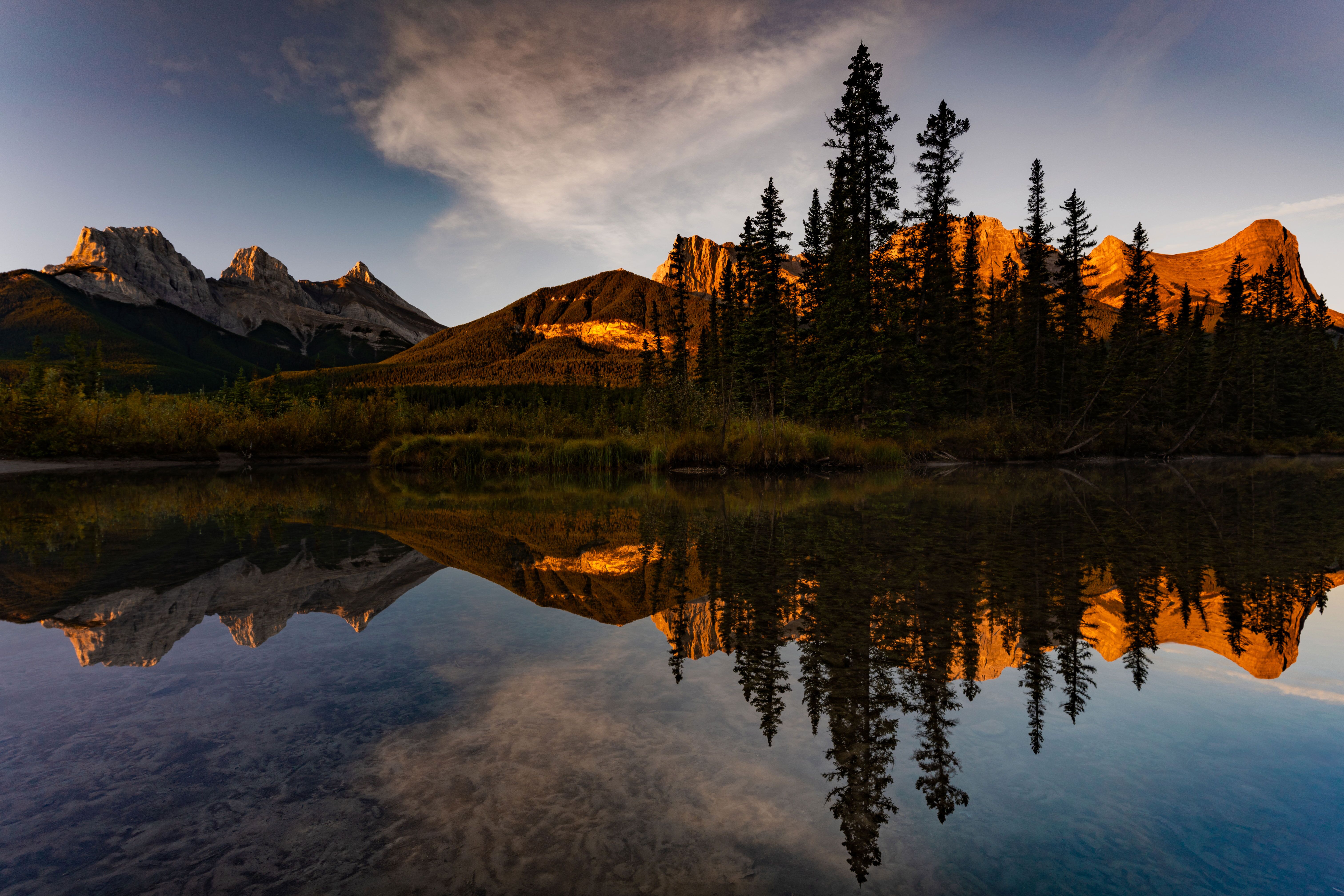 Die im warmen Licht leuchtenden Gipfel der Three Sisters spiegeln sich im ruhigen Wasser bei Canmore in den kanadischen Rocky Mountains Die im warmen Licht leuchtenden Gipfel der Three Sisters spiegeln sich im ruhigen Wasser bei Canmore in den kanadischen Rocky Mountains