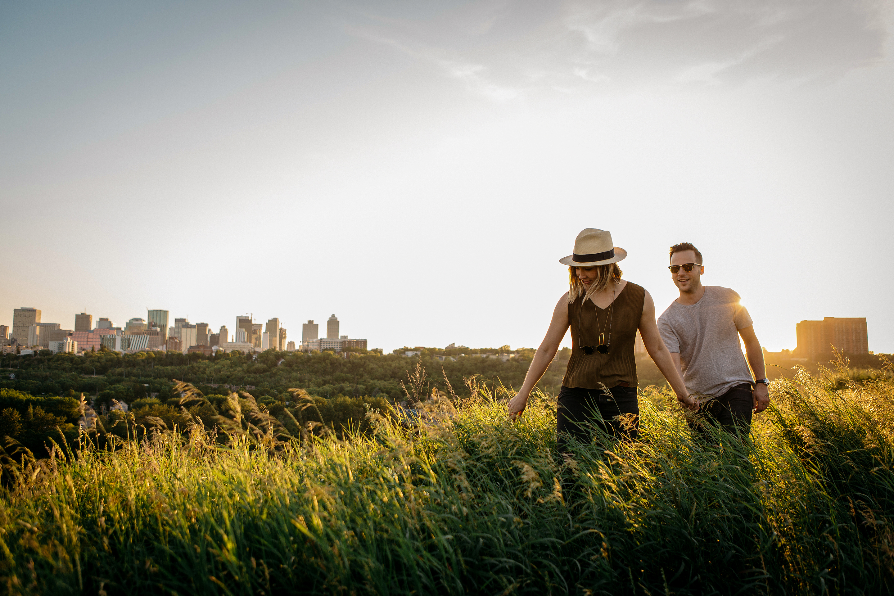 Paar spaziert durch ein Feld mit Edmontons Skyline im Hintergrund