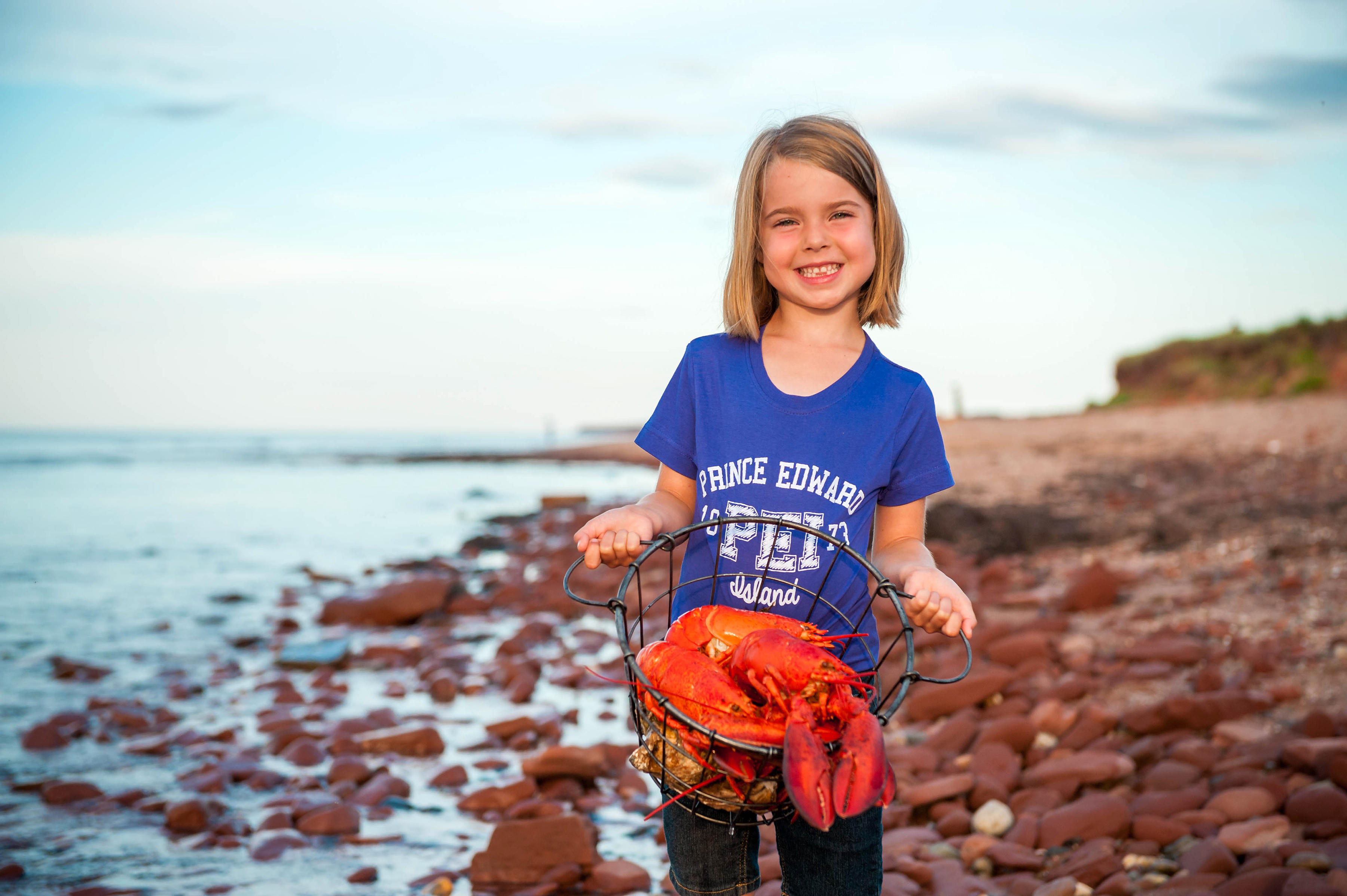 Ein Kind zeigt stolz den frisch gefangenen Hummer am einem Strand von Prince Edward Island