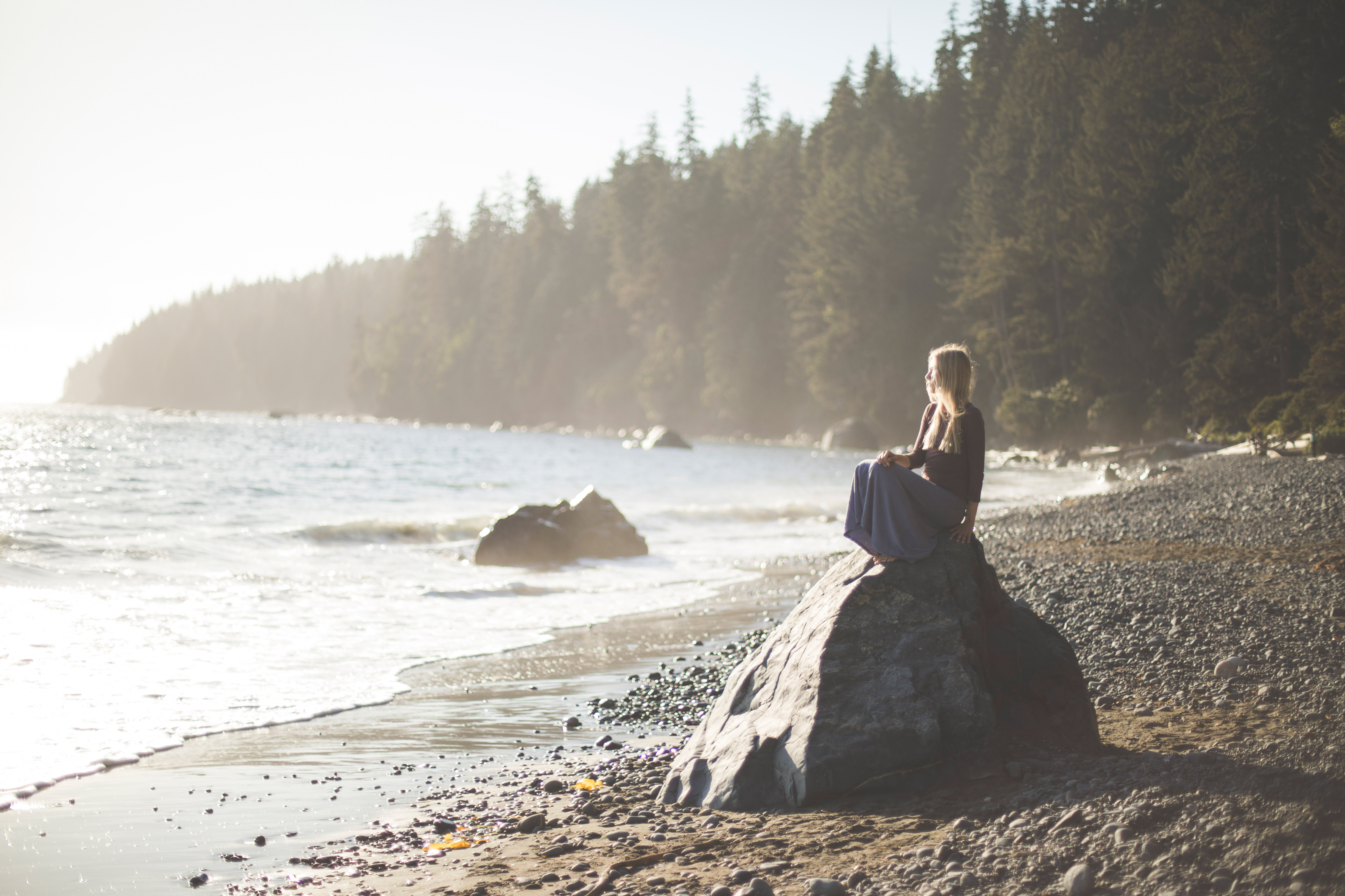 Frau sitzt auf einem Fels und schaut aufs Meer