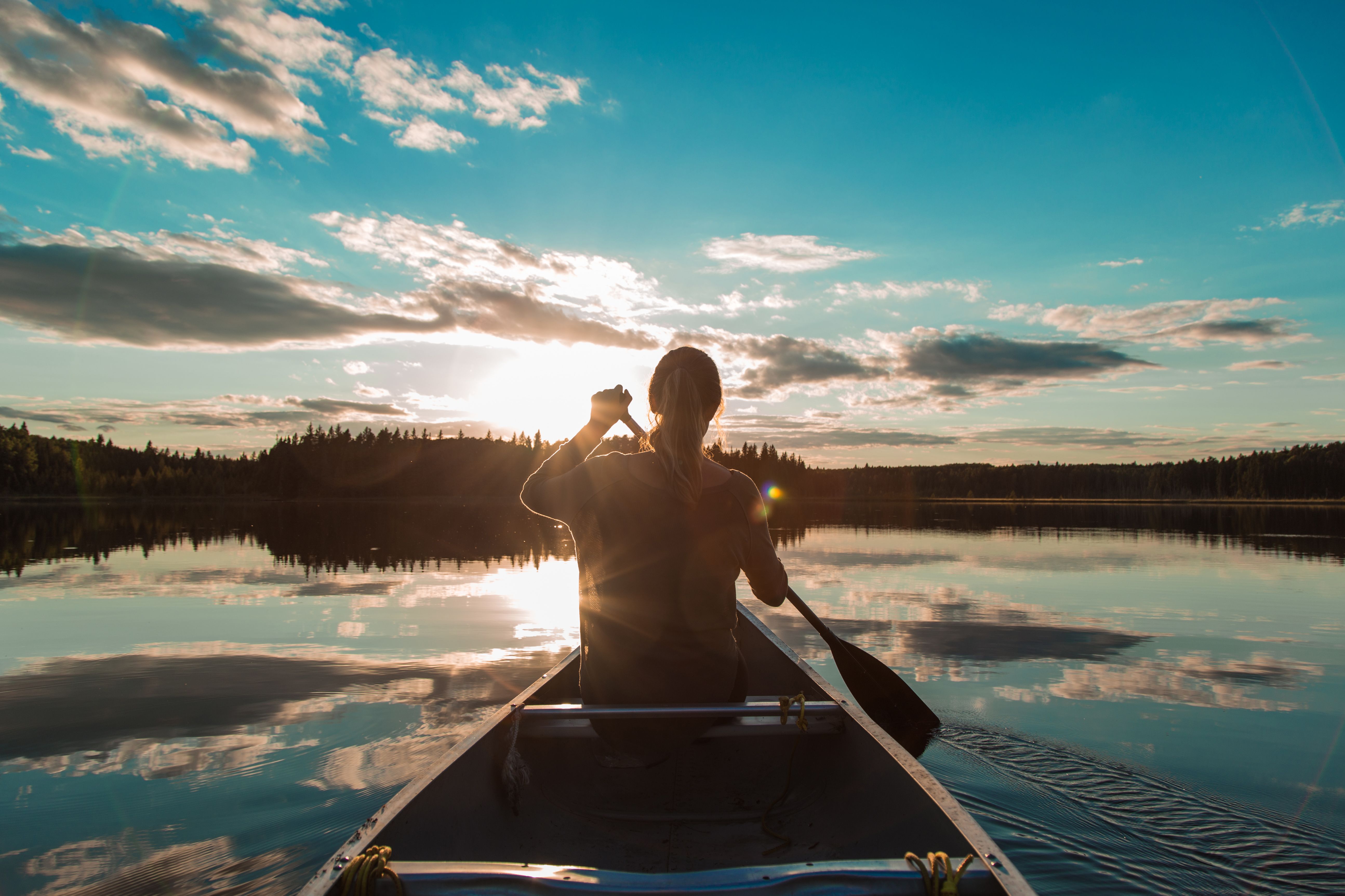 Eine junge Frau steuert ihr Kanu dem Sonnenuntergang entgegen