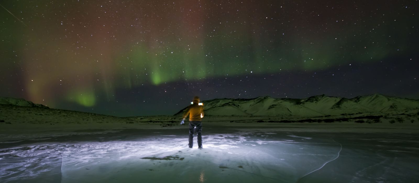 Person auf EisflÃ¤che beobachtet Nordlichter im Yukon