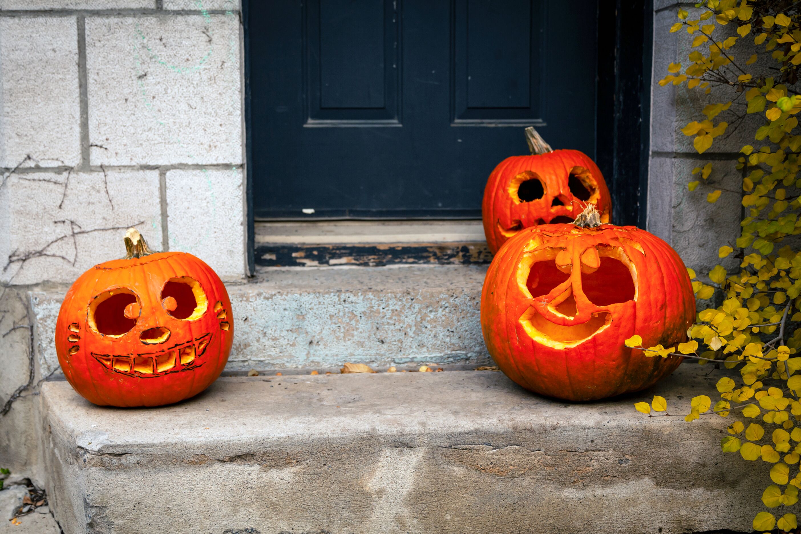 Drei ausgehöhlte Kürbisse mit Fratze schmücken eine Häusertreppe.