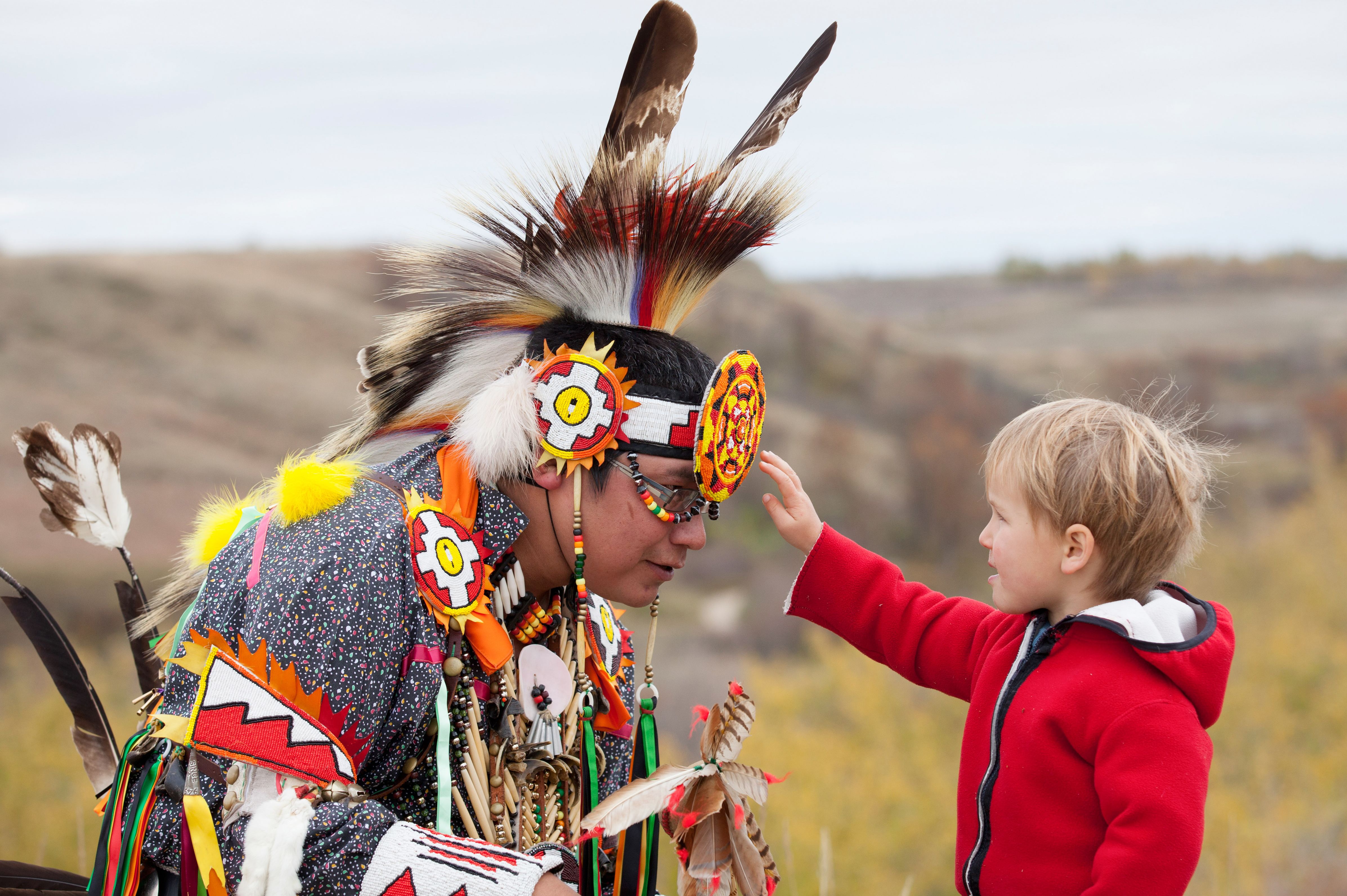 Ein Kind begutachtet einen Ureinwohner in traditioneller Tracht im Wanuskewin Heritage Park