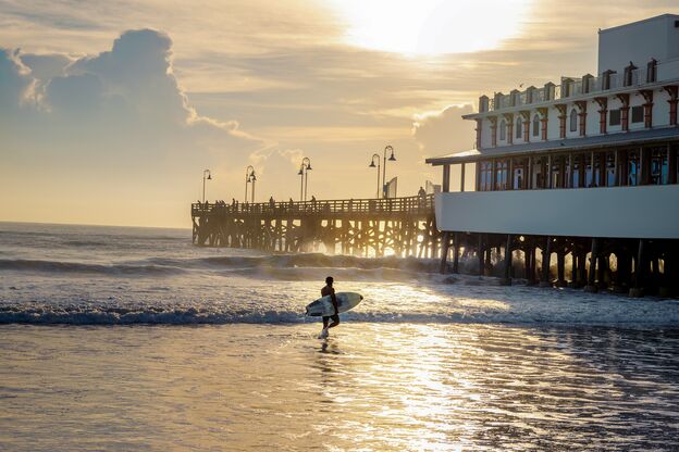 Surfer läuft bei Sonnenuntergang am Pier von Daytona Beach entlang