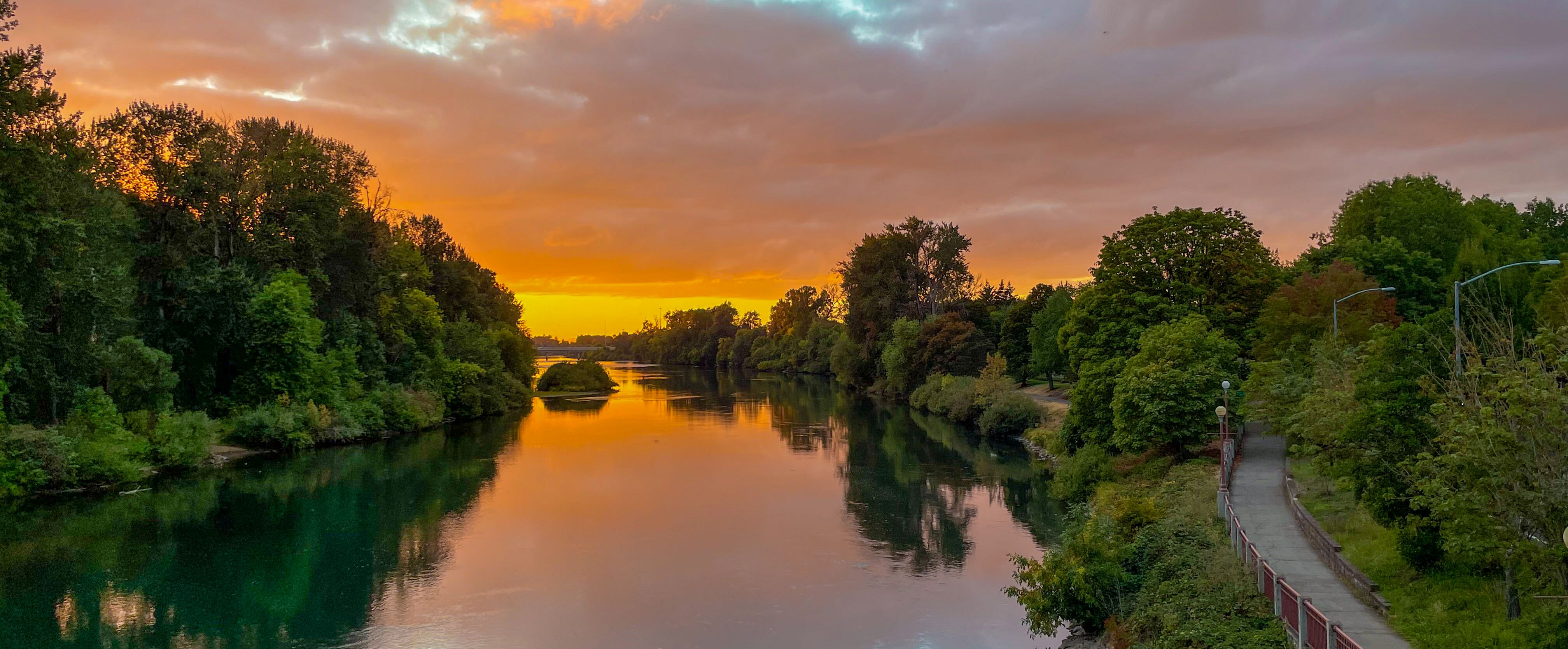 Blick auf den von Bäumen gesäumten Willamette River in Eugene bei Sonnenuntergang