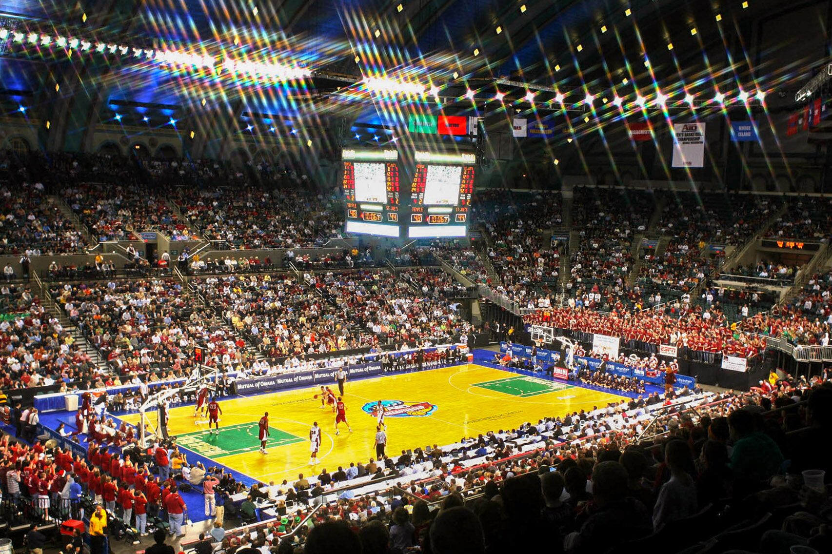 Ein Basketballspiel in einer vollbesetzten Arena mit vielen Zuschauern und einer großen Anzeigetafel in der Mitte der Halle.
