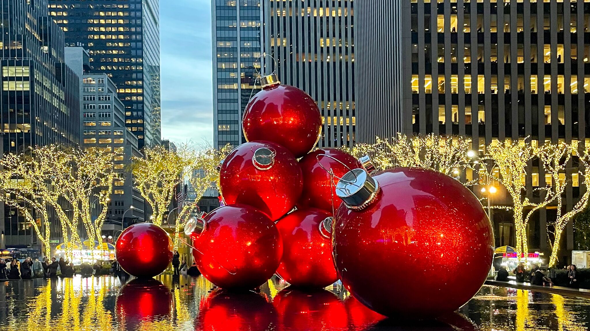 Übergroße, rote Weihnachtskugel sind zwischen Wolkenkratzern auf einem Platz in New York in Szene gesetzt.