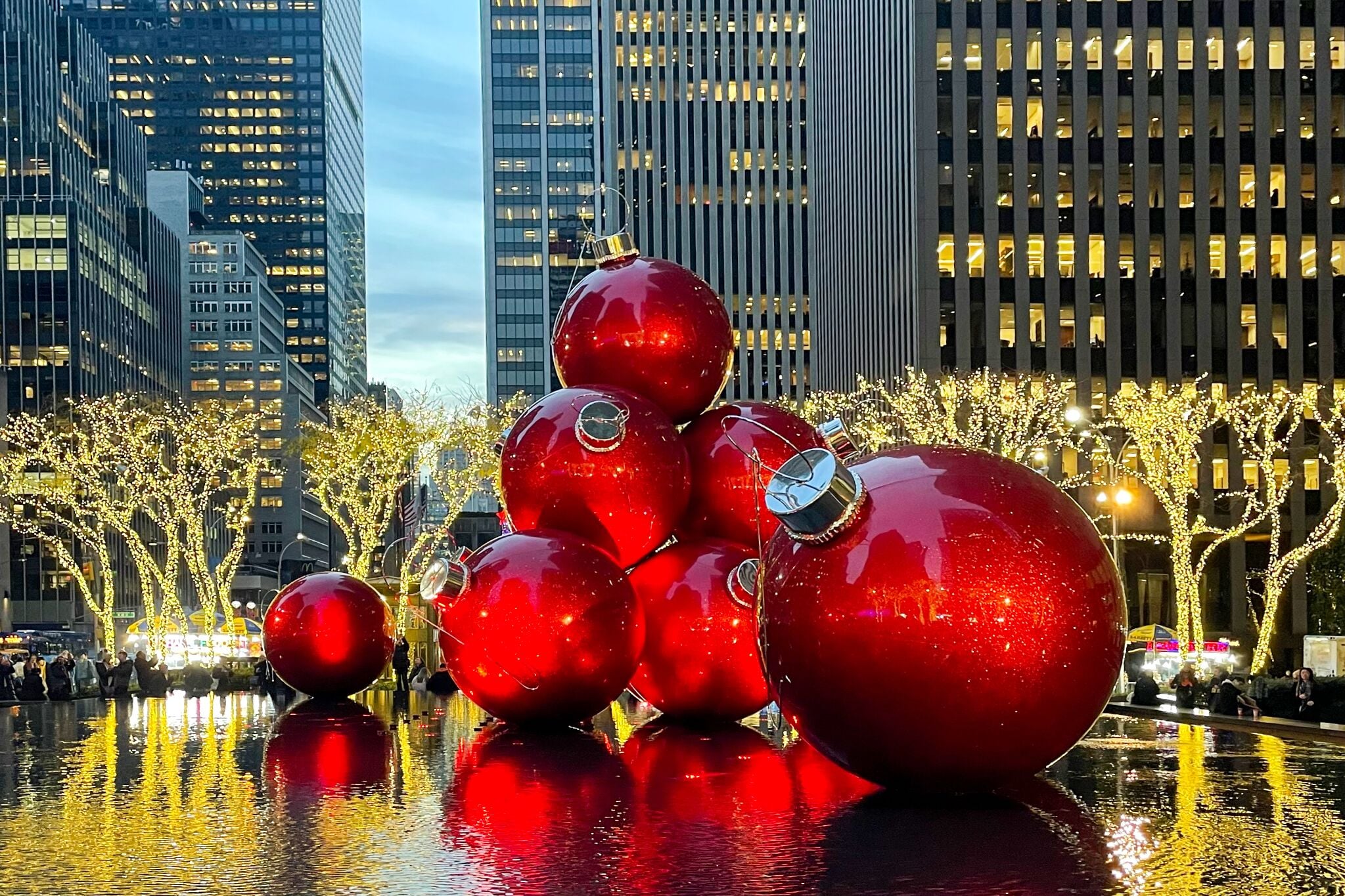 Übergroße, rote Weihnachtskugel sind zwischen Wolkenkratzern auf einem Platz in New York in Szene gesetzt.