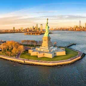 Die Freiheitsstatue im Abendlicht mit Blick auf die Skyline von New York