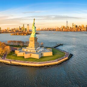 Die Freiheitsstatue im Abendlicht mit Blick auf die Skyline von New York