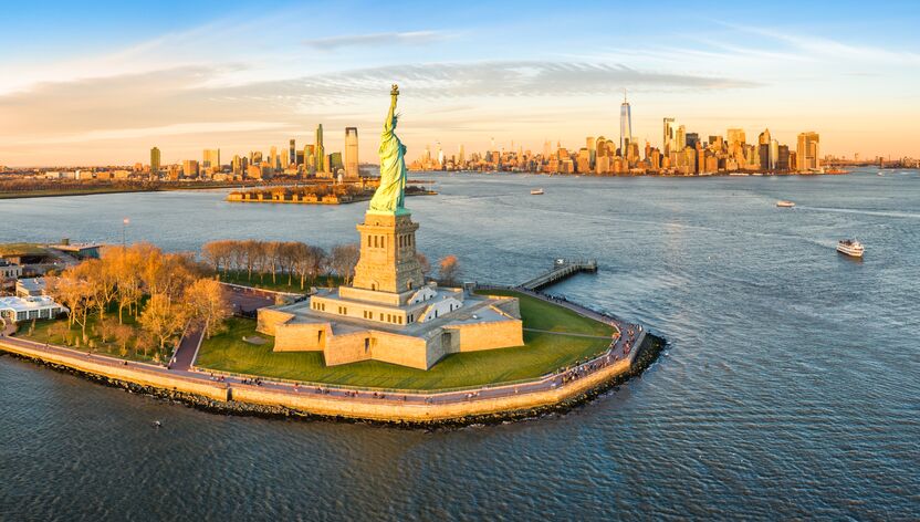 Die Freiheitsstatue im Abendlicht mit Blick auf die Skyline von New York Die Freiheitsstatue im Abendlicht mit Blick auf die Skyline von New York