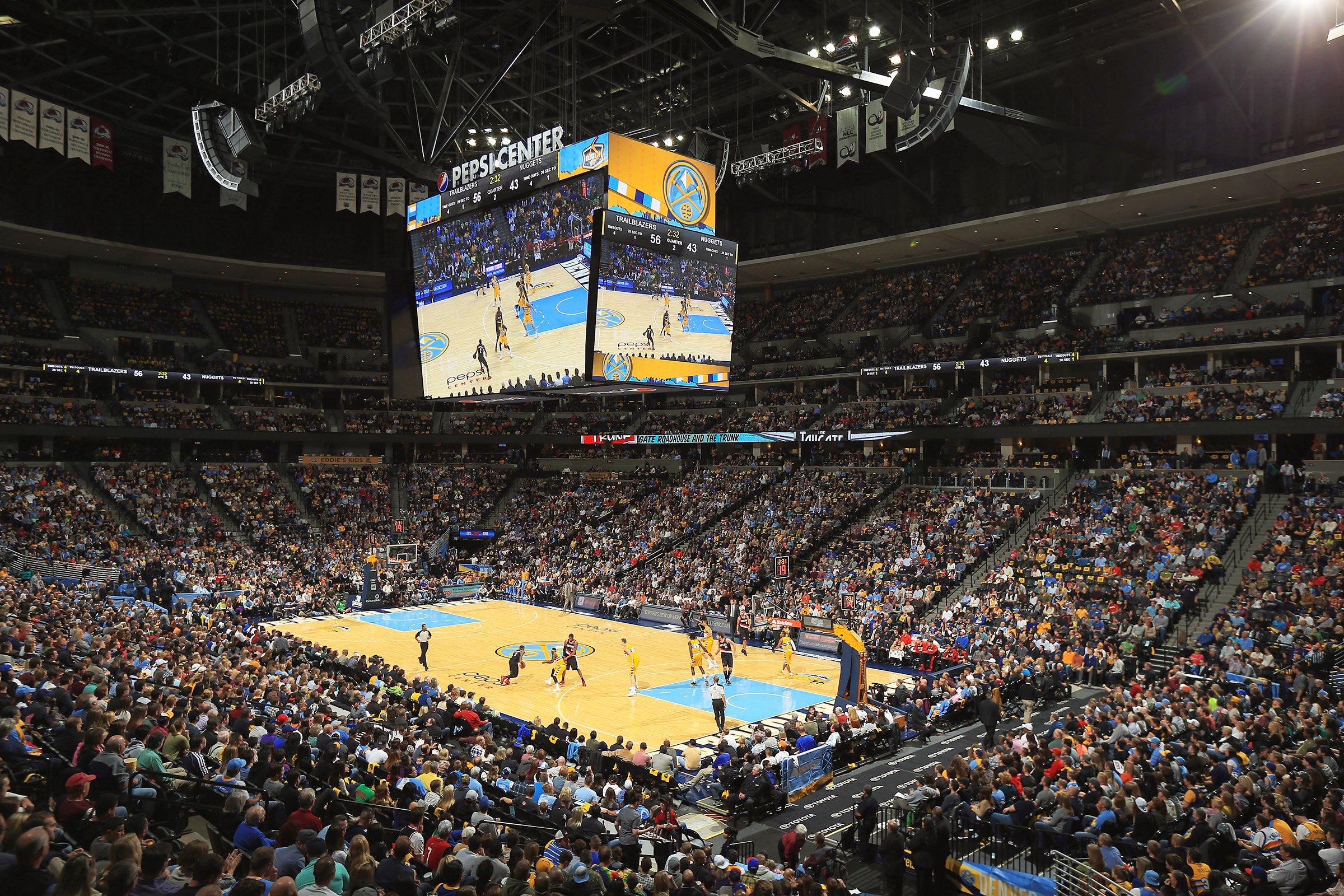 Volle Arena beim NBA-Basketballspiel der Denver Nuggets. Auf dem Spielfeld sind Spieler aktiv, während auf dem großen Bildschirm Spielszenen übertragen werden.