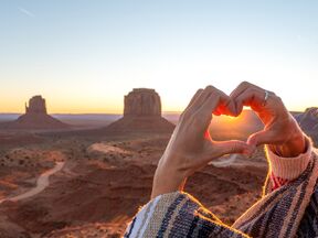 Eine Frau formt ein Herz vor dem Monument Valley