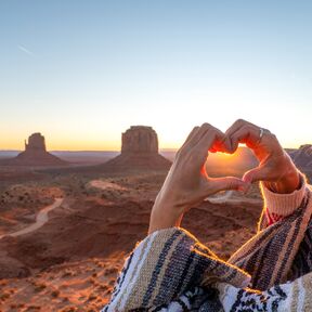 Eine Frau formt ein Herz vor dem Monument Valley