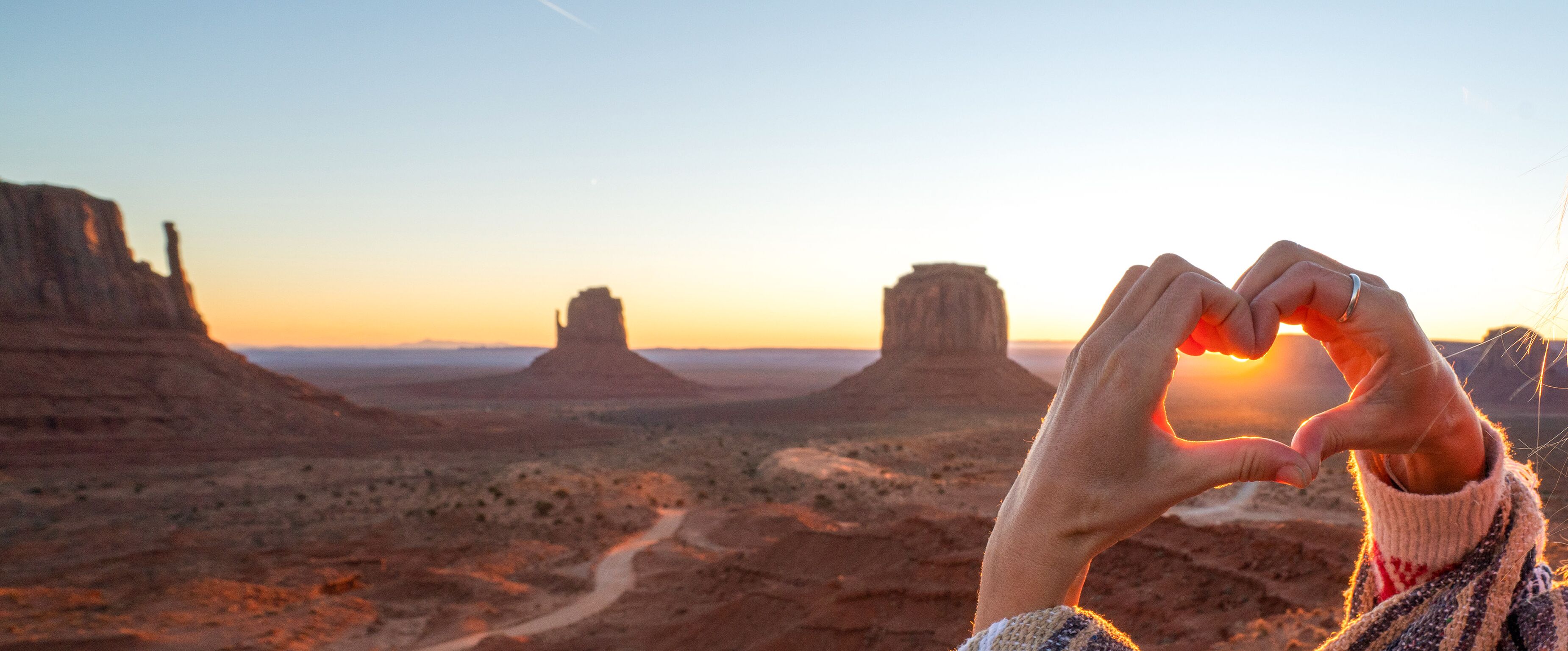 Eine Frau formt ein Herz vor dem Monument Valley