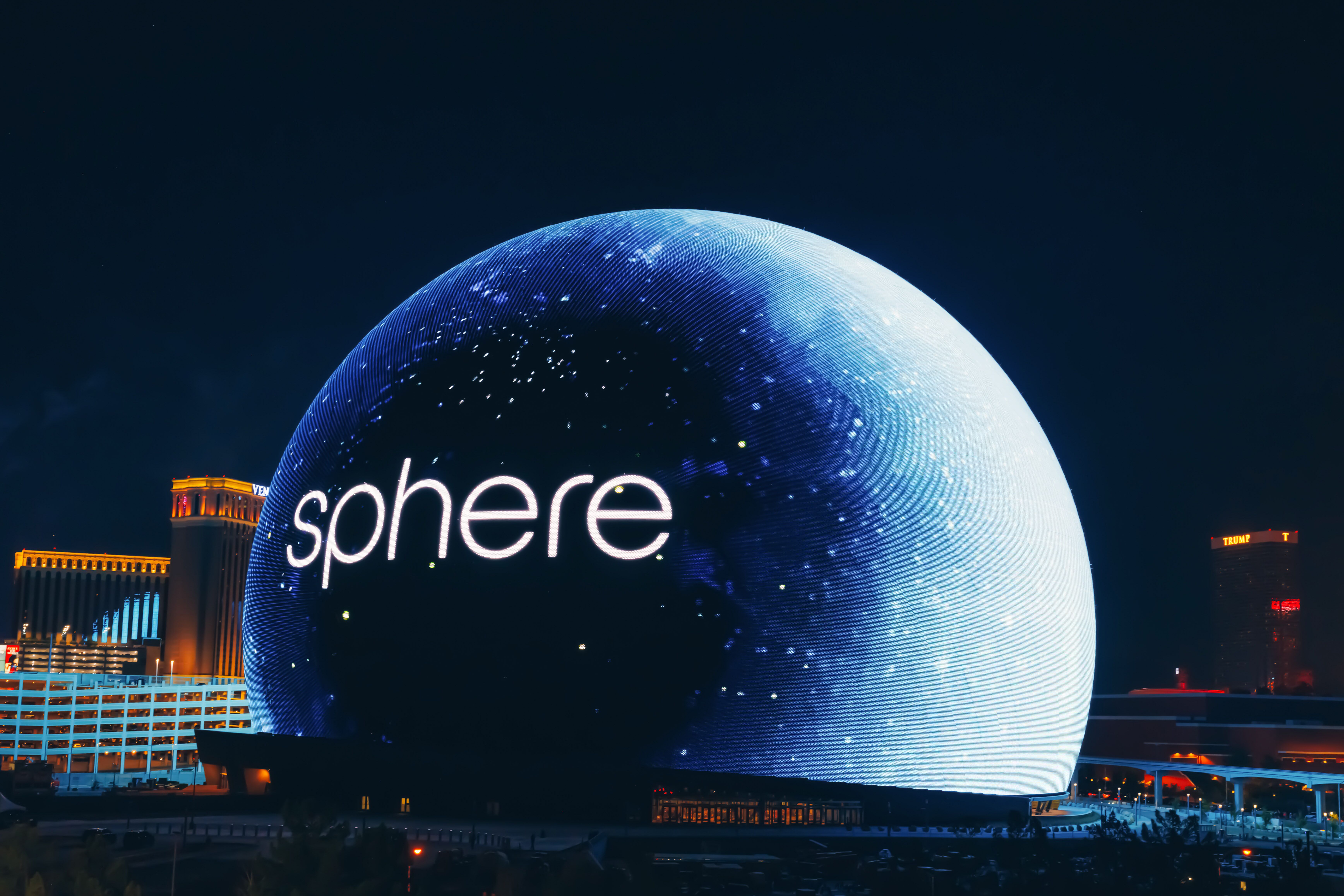 Die Sphere bei Nacht mit ihrem Namen als Schriftzug, im Hintergrund beleuchtete Gebäude