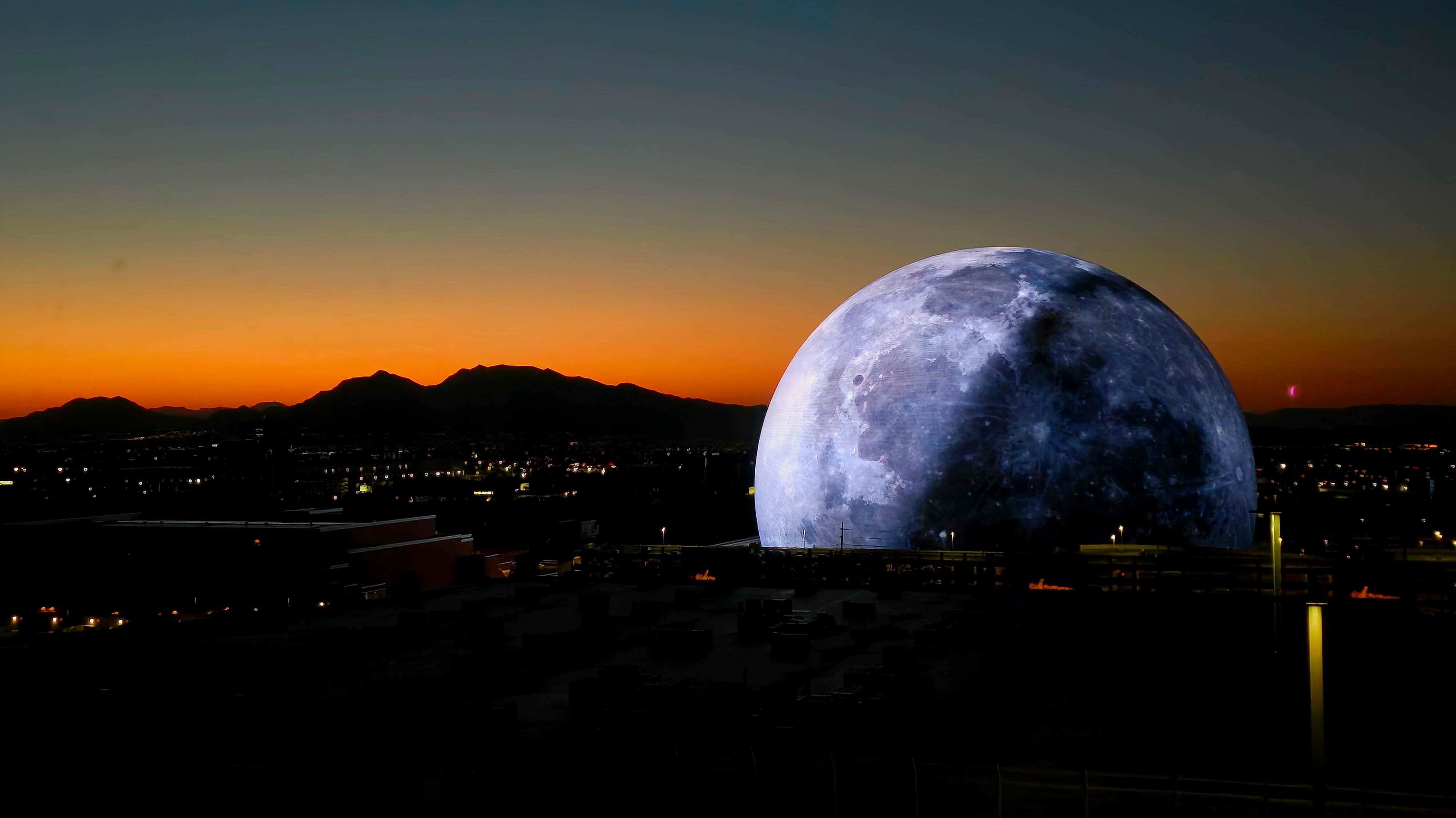 Die Sphere Arena in Las Vegas zeigt eine realistische Mondoberfläche, im Hintergrund ein Sonnenaufgang über der Stadt.
