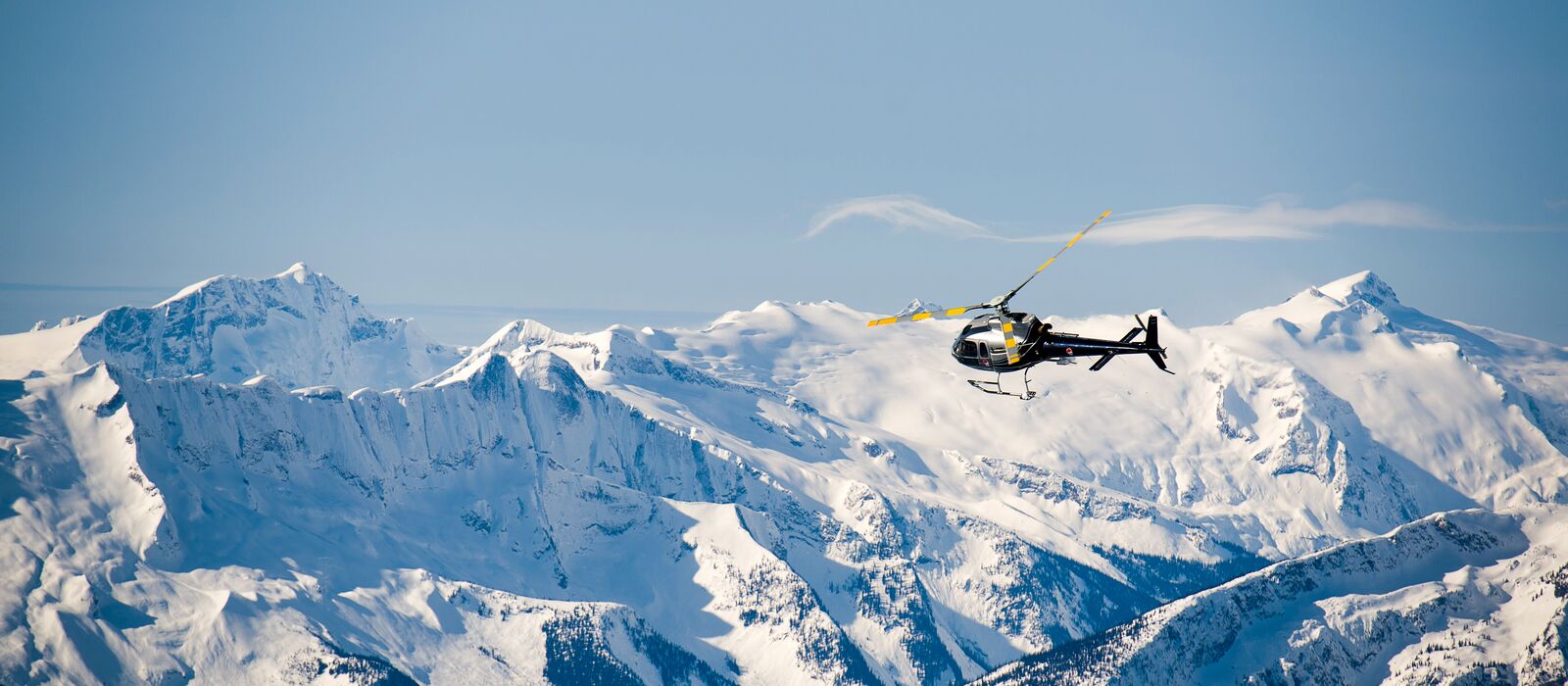Ein Hubschrauber von Selkirk Helicopter Skiing in Revelstoke, British Columbia fliegt über eine Bergkette Ein Hubschrauber von Selkirk Helicopter Skiing in Revelstoke, British Columbia fliegt über eine Bergkette
