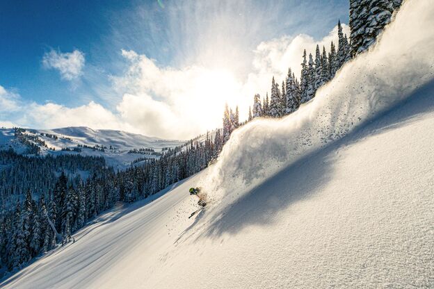 Skifahrer fährt einen Berg in Whistler, British Coumbia bei strahlendem Sonnenschein im feinsten Powder hinunter