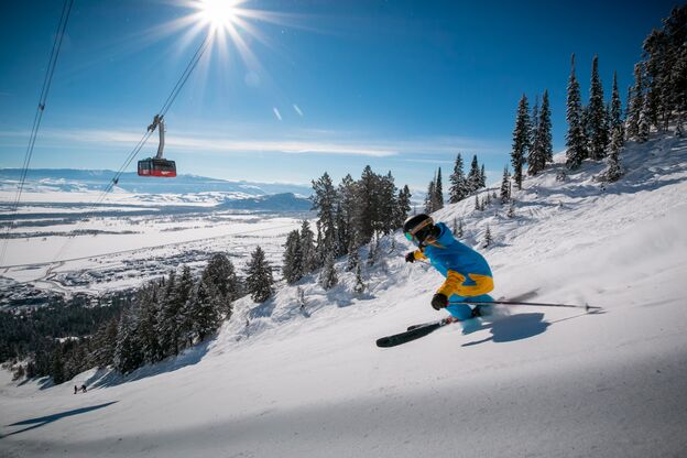 Eine Skifahrerin auf der Piste mit einer Gondel im Hintergrund in Jackson Hole, Wyoming Eine Skifahrerin auf der Piste mit einer Gondel im Hintergrund in Jackson Hole, Wyoming