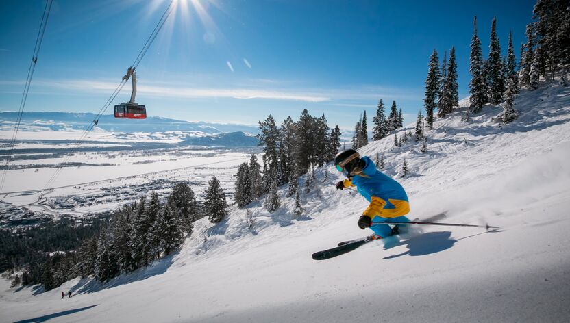 Eine Skifahrerin auf der Piste mit einer Gondel im Hintergrund in Jackson Hole, Wyoming Eine Skifahrerin auf der Piste mit einer Gondel im Hintergrund in Jackson Hole, Wyoming